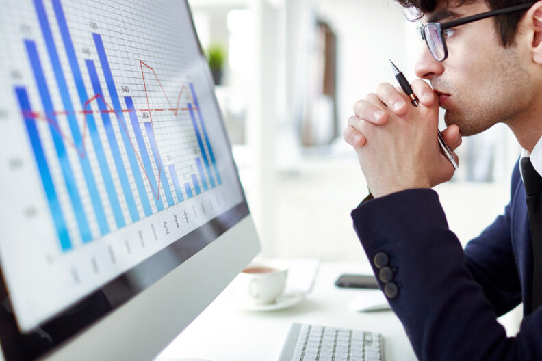 Seitenansicht eines nachdenklichen Mannes, der das Finanzdiagramm auf dem Computermonitor betrachtet